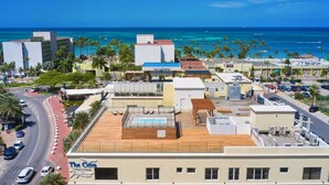 A hotel with a rooftop pool, a view of the ocean, and a parking area with cars. - Luxury 3 Bed Palm Beach Strip Condo! (Noord)