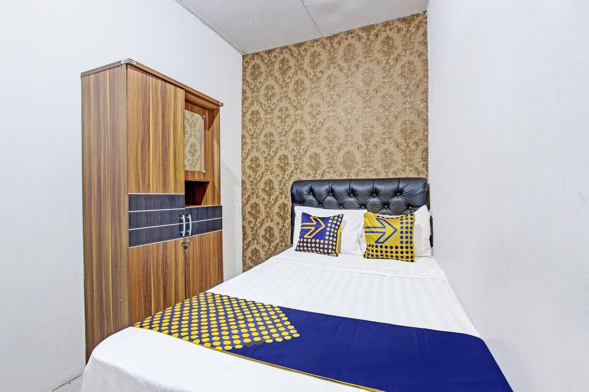 Quarto com cama, guarda-roupa de madeira e papel de parede estampado.