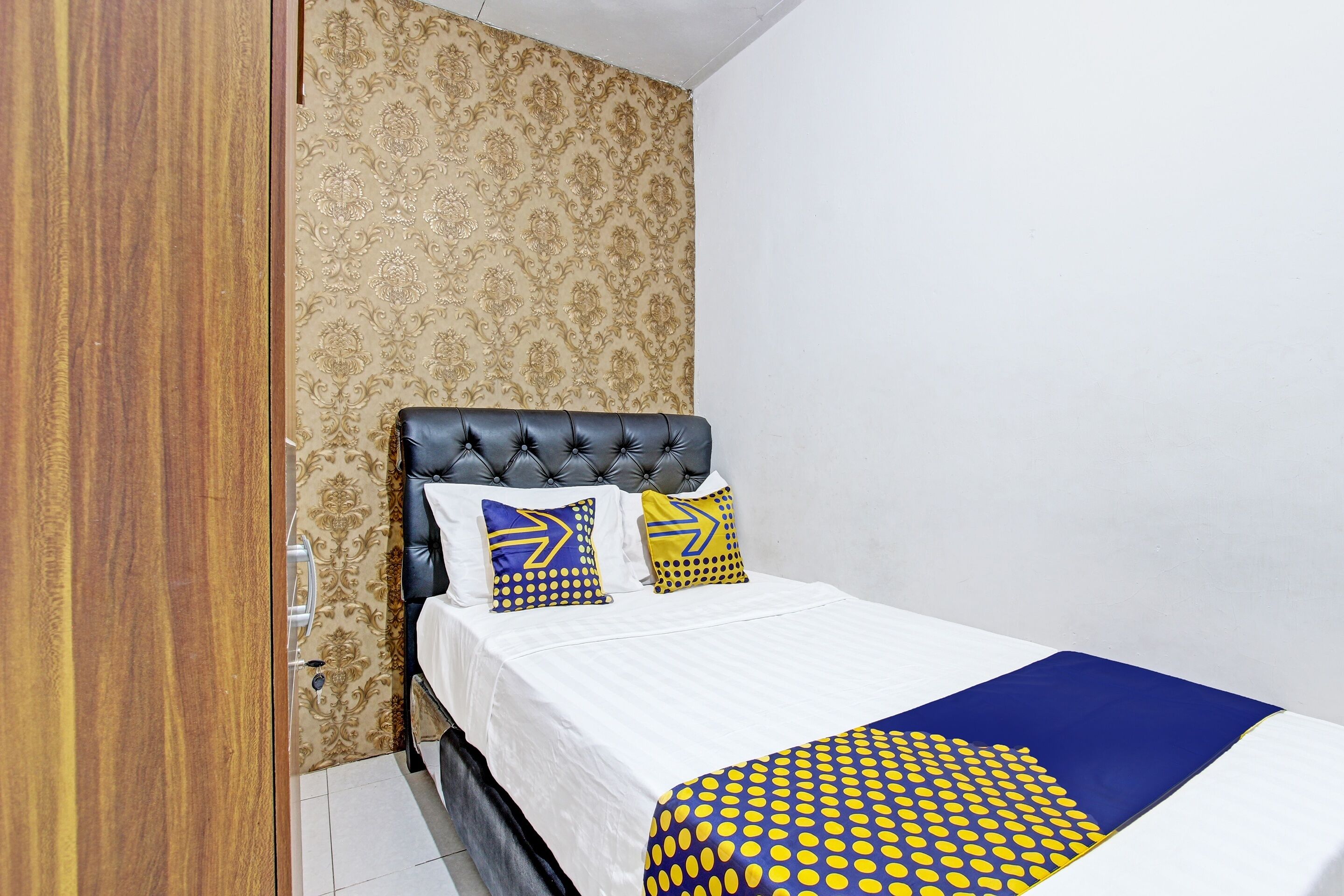 A bedroom with a bed, patterned wallpaper, and a wooden wardrobe.