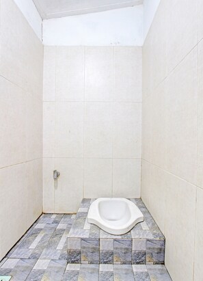 Un baño pequeño con azulejos, un váter de pedestal, una zona de ducha y suelo de cerámica.