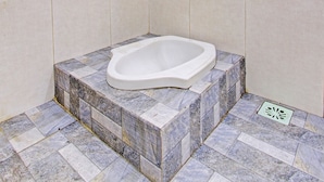 A small, tiled bathroom with a white bathtub, a yellow warning sign, and a drain cover. - SPOT ON 91521 Mayong Guesthouse (Mayong)