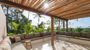 A covered outdoor seating area with a wooden ceiling, a built-in bench with cushions, and a small round table. - Sealuna Villas (Tabanan)