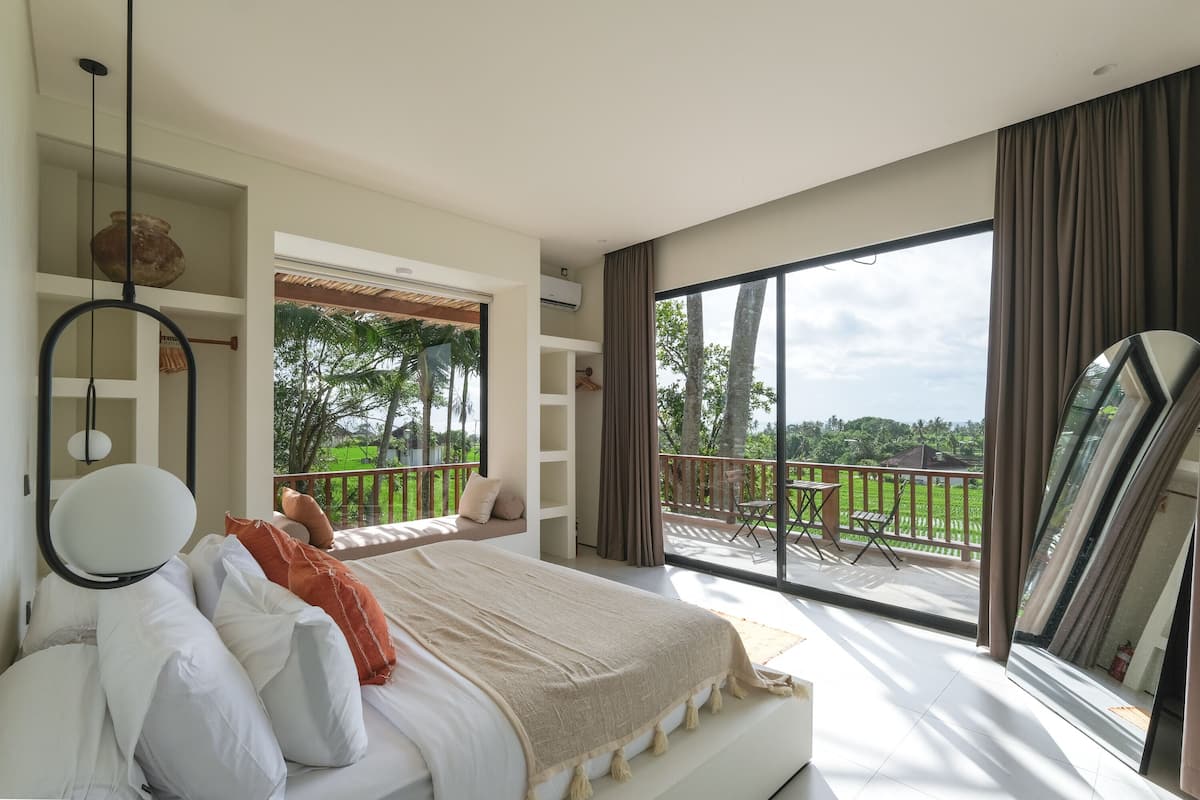 Une chambre moderne avec un grand lit, un balcon donnant sur un espace verdoyant et une porte-fenêtre coulissante.