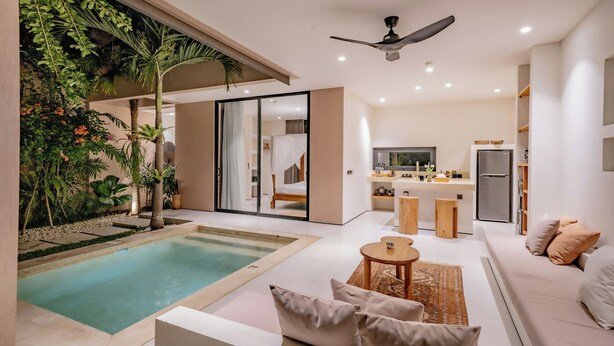 A modern living area with a pool, a sofa, a dining table, and a kitchen in the background. - Sealuna Villas (Tabanan)