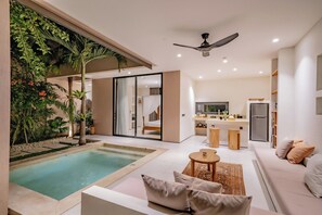Un espacio moderno con piscina, sofá, mesa de comedor y cocina al fondo.