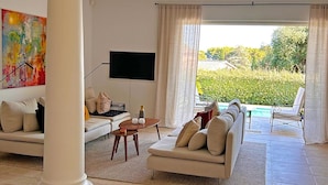 A modern living room with a sofa set, a coffee table, and a flat-screen TV. There is a view of a pool and greenery outside. - Large fantastic house with a garden, a pool and beautiful views (Vence)