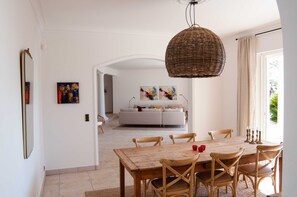 A dining area with a wooden table and chairs, a wicker pendant light, and a white sofa in the background. - Large Fantastic House With a Garden, a Pool and Beautiful Views (Vence)