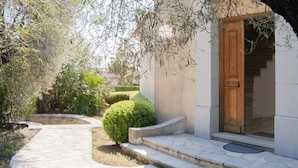 A pathway leading to a building with a wooden door, surrounded by greenery and a stone wall. - Large fantastic house with a garden, a pool and beautiful views (Vence)