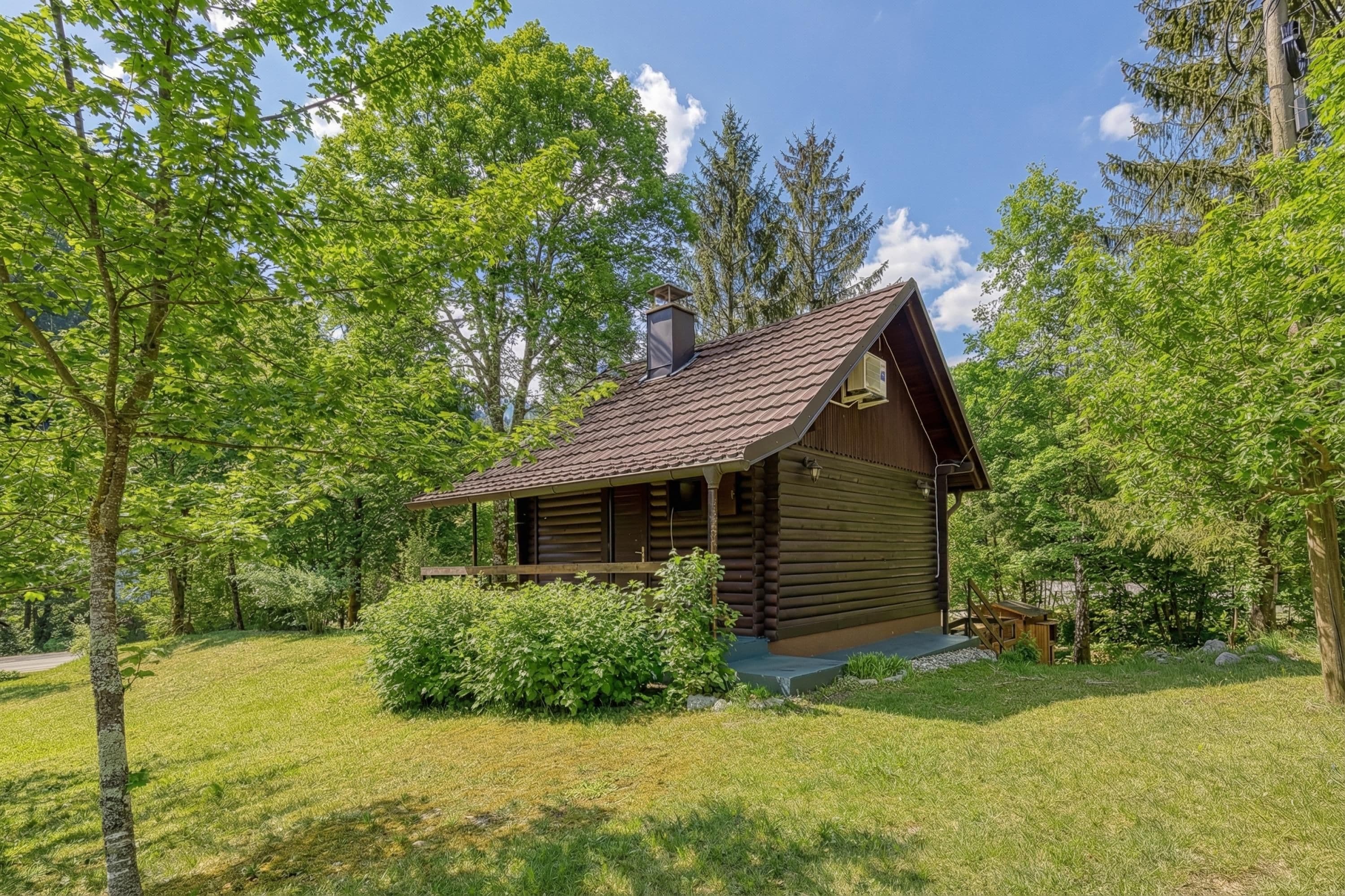 A log cabin with a sloped roof, surrounded by a grassy area and trees.