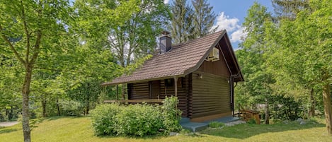 A log cabin with a sloped roof, surrounded by a grassy area and trees.