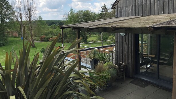 Een houten gebouw met een overdekte patio, plantenbakken en uitzicht op een groen landschap.