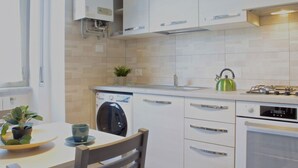 A modern kitchen with white cabinets, a dishwasher, a stove, and a kettle. - GuestHost - Casa Matabù - luminoso bilocale x3 (Cernusco sul Naviglio)
