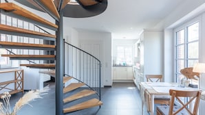 Eine moderne Küche mit weißen Schränken, ein Essbereich mit Holzmöbeln und eine Treppe mit Holzstufen und Metallgeländern.