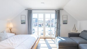 Ein modernes Schlafzimmer mit großem Fenster, einem Bett, einer Couch und einem kleinen Tisch mit Lampe.