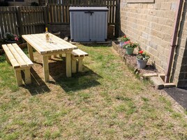 Mesa de picnic de madera con bancos en un patio trasero con pared de ladrillo y plantas en macetas.