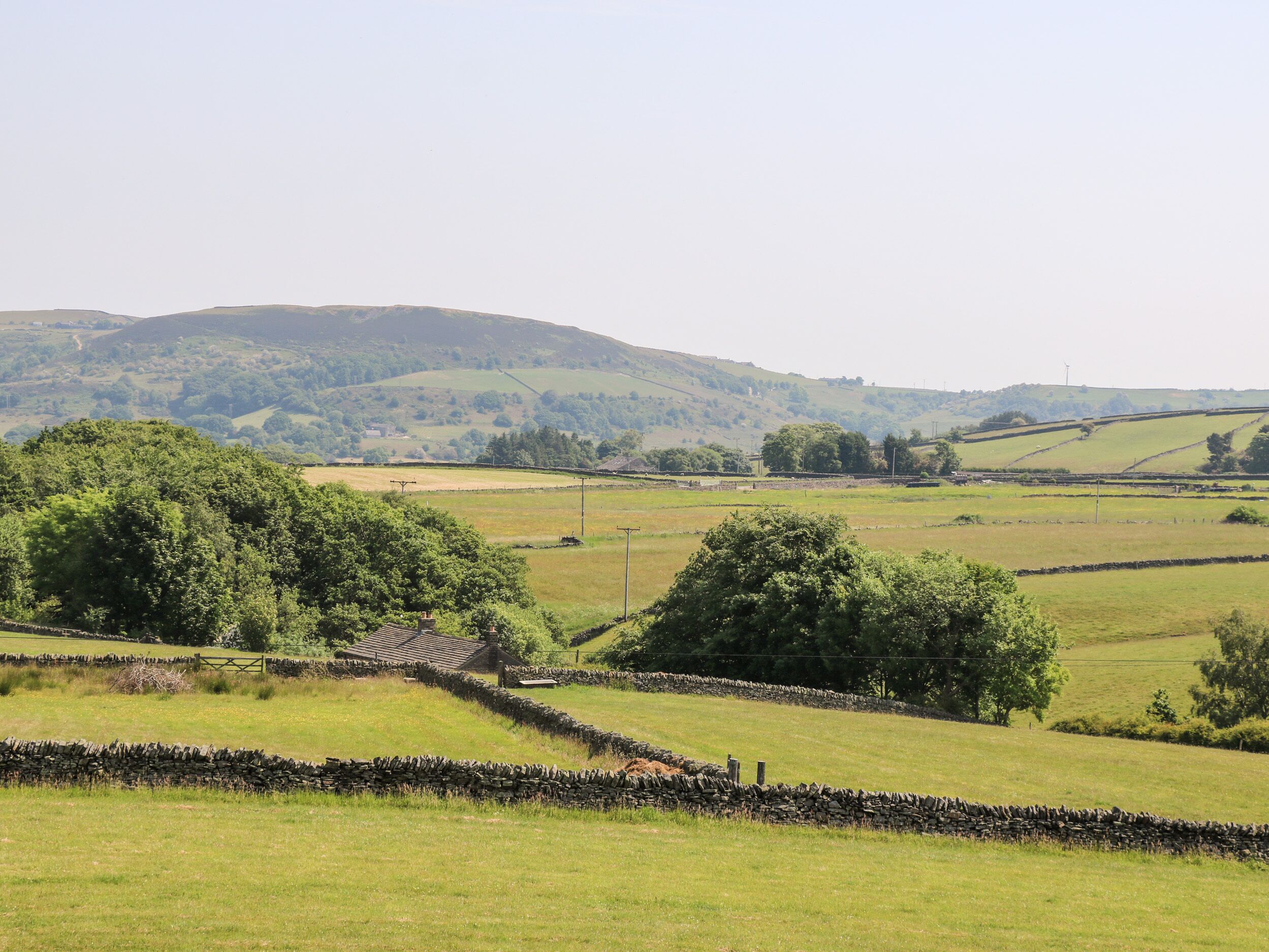 A rural landscape with rolling hills, stone walls, and a small building with a sloped roof.