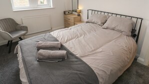 Un dormitorio con una cama, una silla, una mesita de noche con lámpara y una ventana.