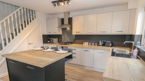 Una cocina moderna con una isla central, armarios blancos y encimera de madera.