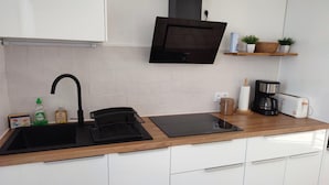 Une cuisine moderne avec des meubles blancs, un plan de travail noir, un micro-ondes encastré, une machine à café et une petite étagère avec des plantes.