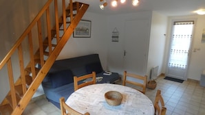 Un salon avec un escalier en bois, une table à manger ronde et un canapé bleu.