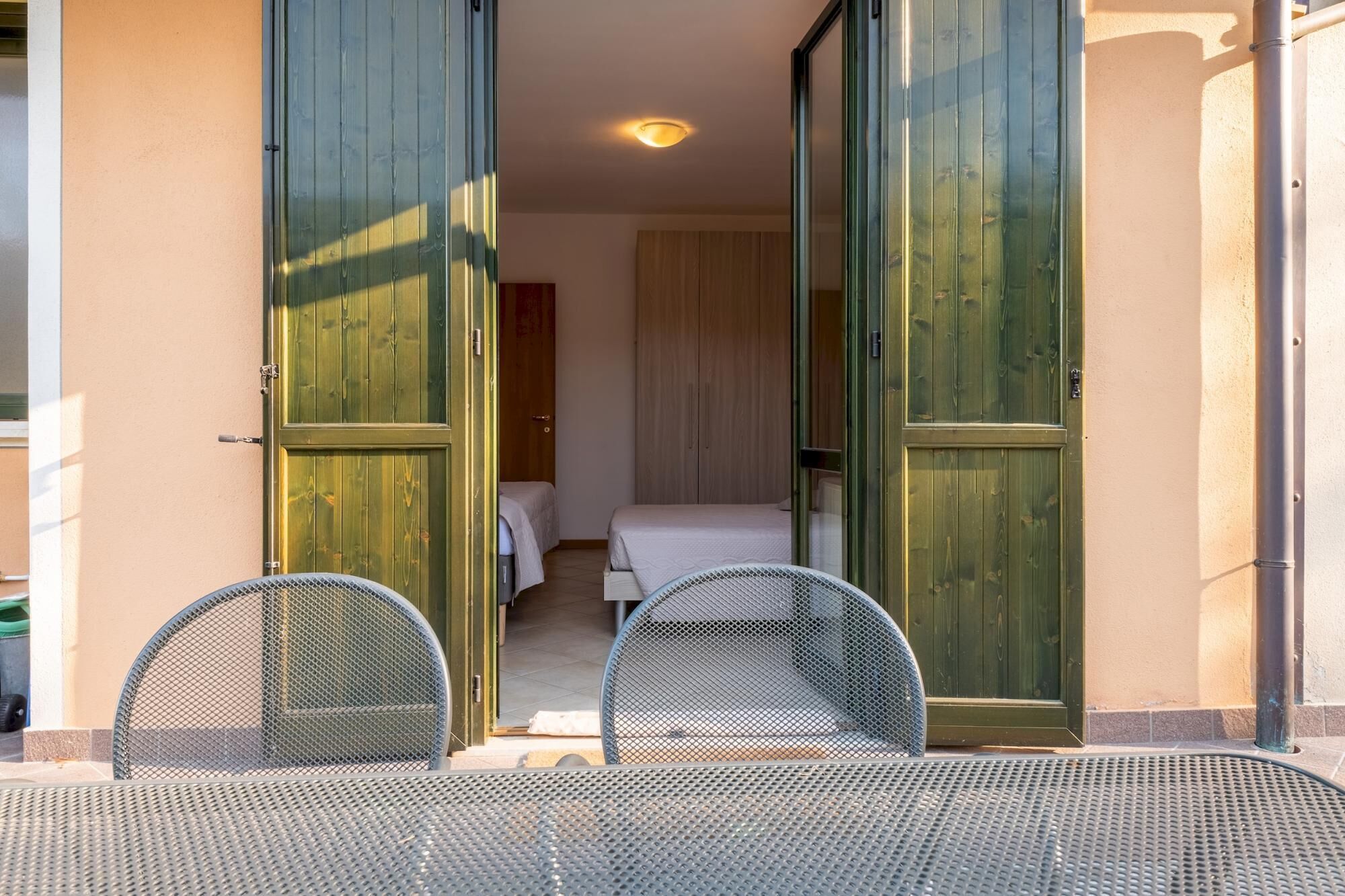 A room with a bed, a wardrobe, and a balcony with two chairs.