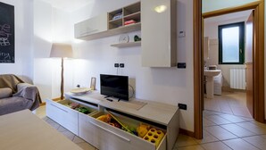 A modern living room with a flat-screen TV, a sofa, a lamp, and a built-in storage unit with drawers. - Appartamento Leone in Vertine (Sulzano)