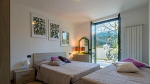 A bedroom with two beds, a nightstand, a dresser, and a mirror. There are framed pictures on the wall, and a window with a view of the outdoors. - Appartamento Leone in Vertine (Sulzano)