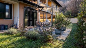 A two-story house with a covered outdoor seating area, a staircase, and a garden with various plants. - Appartamento Leone in Vertine (Sulzano)