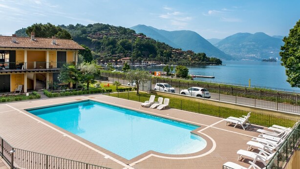 A swimming pool with lounge chairs, a view of a lake, and a building with a balcony. - Appartamento Leone in Vertine (Sulzano)