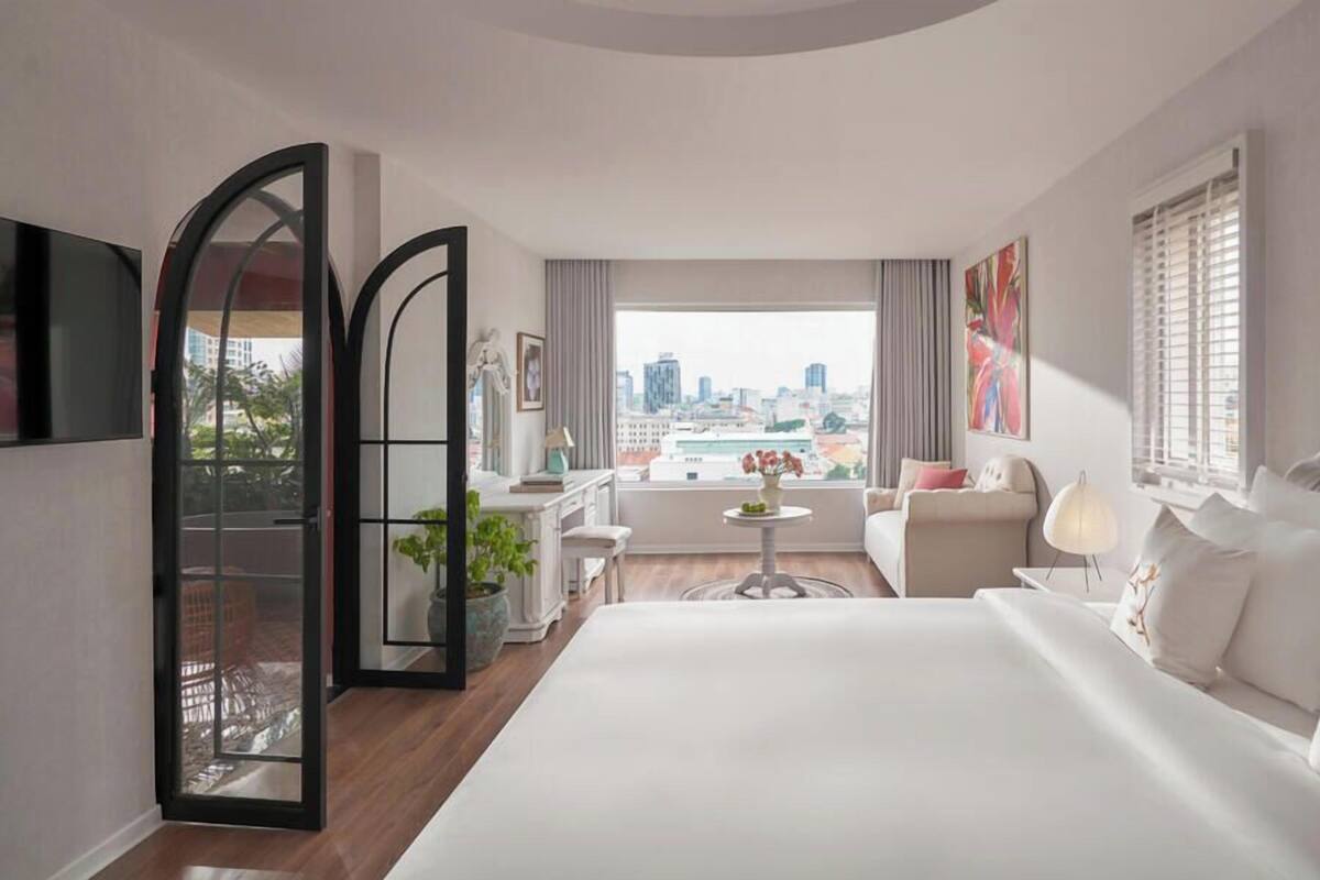 Quarto de hotel com uma cama grande, um sofá, uma mesinha e vista para a cidade.