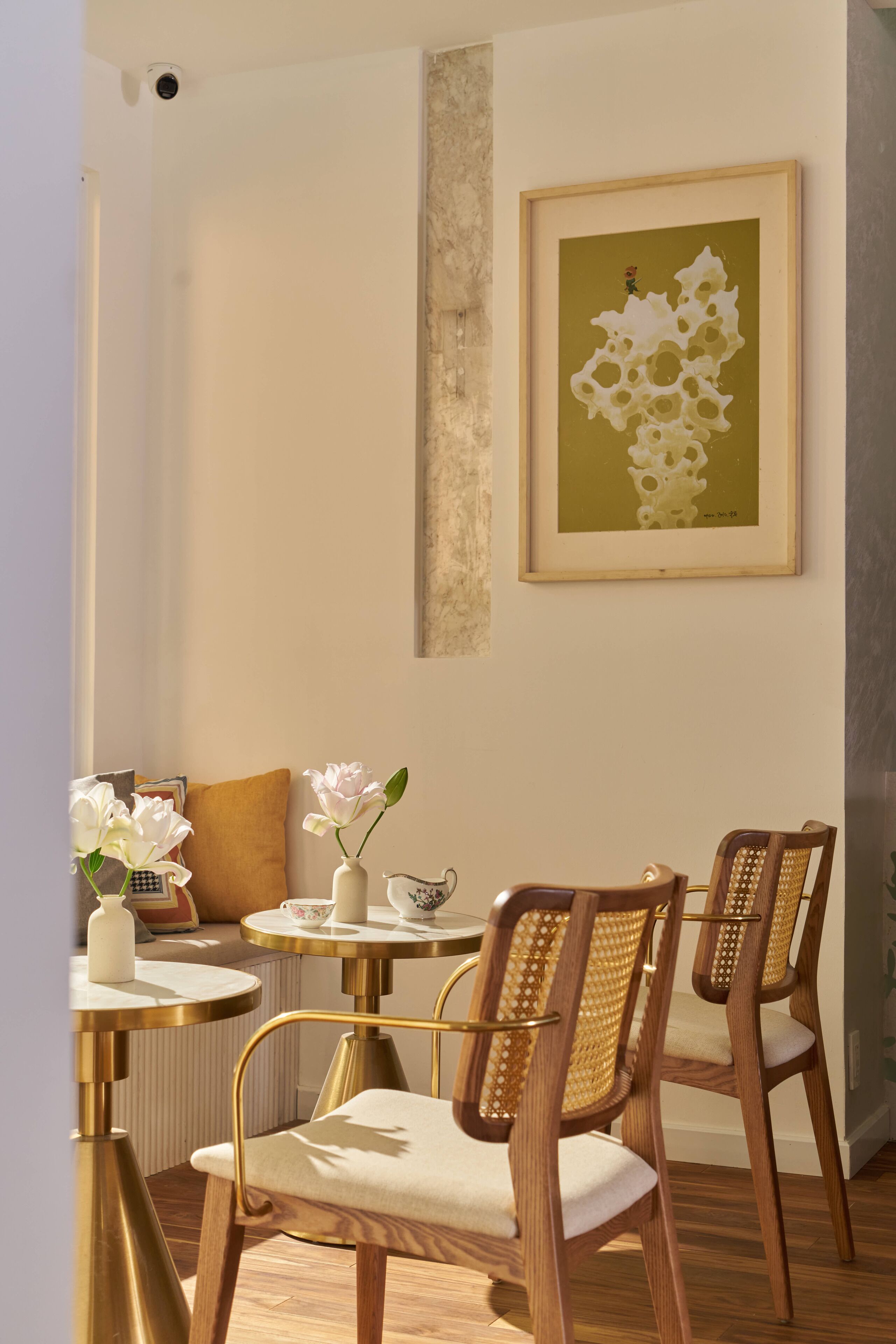 A dining area with a round table, two chairs, a vase with flowers, and a framed artwork on the wall.