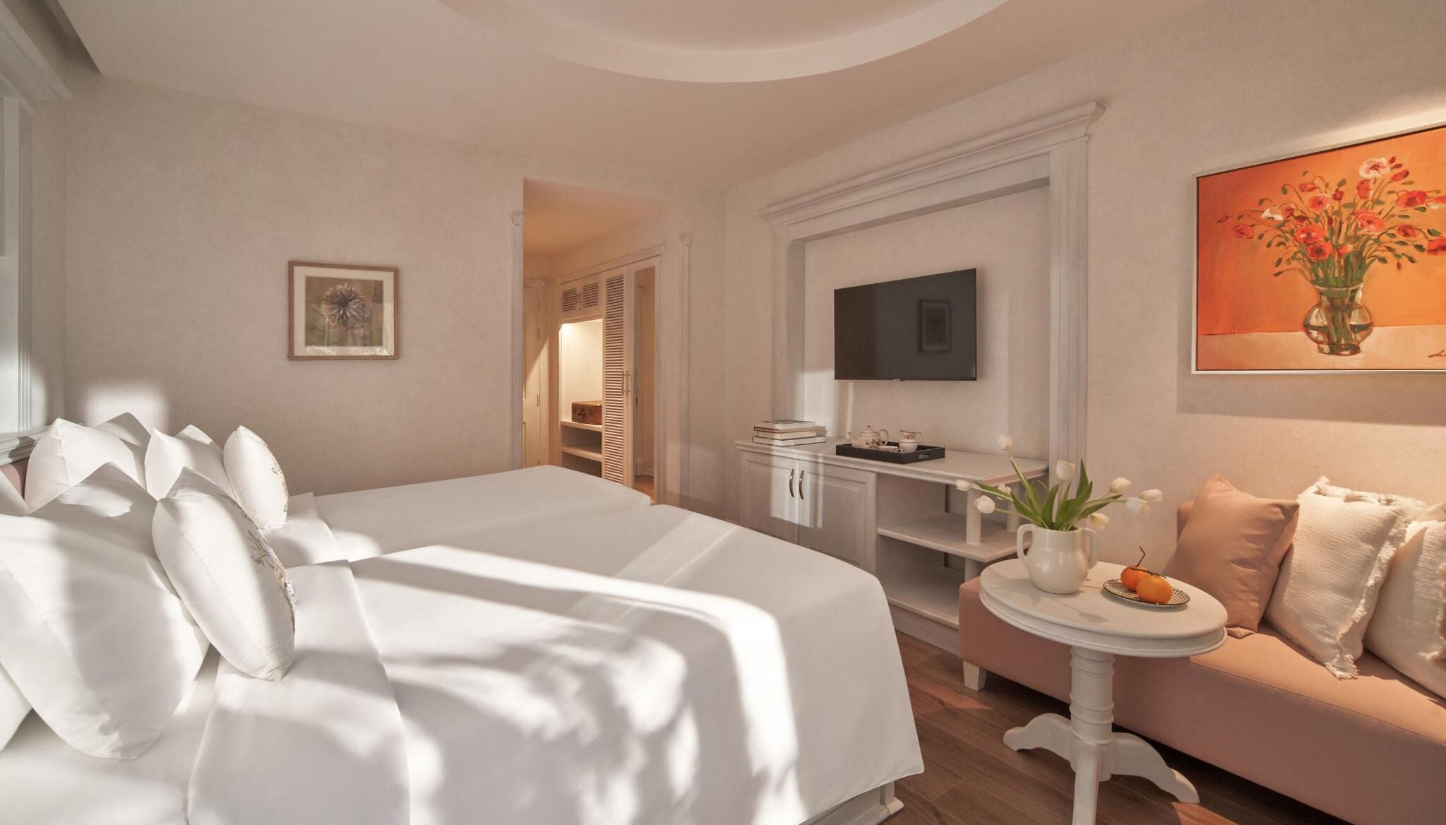 A hotel room with a large bed, a small table with a vase of flowers, a television, and a sofa.
