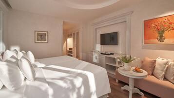 A hotel room with a large bed, a small table with a vase of flowers, a television, and a sofa.