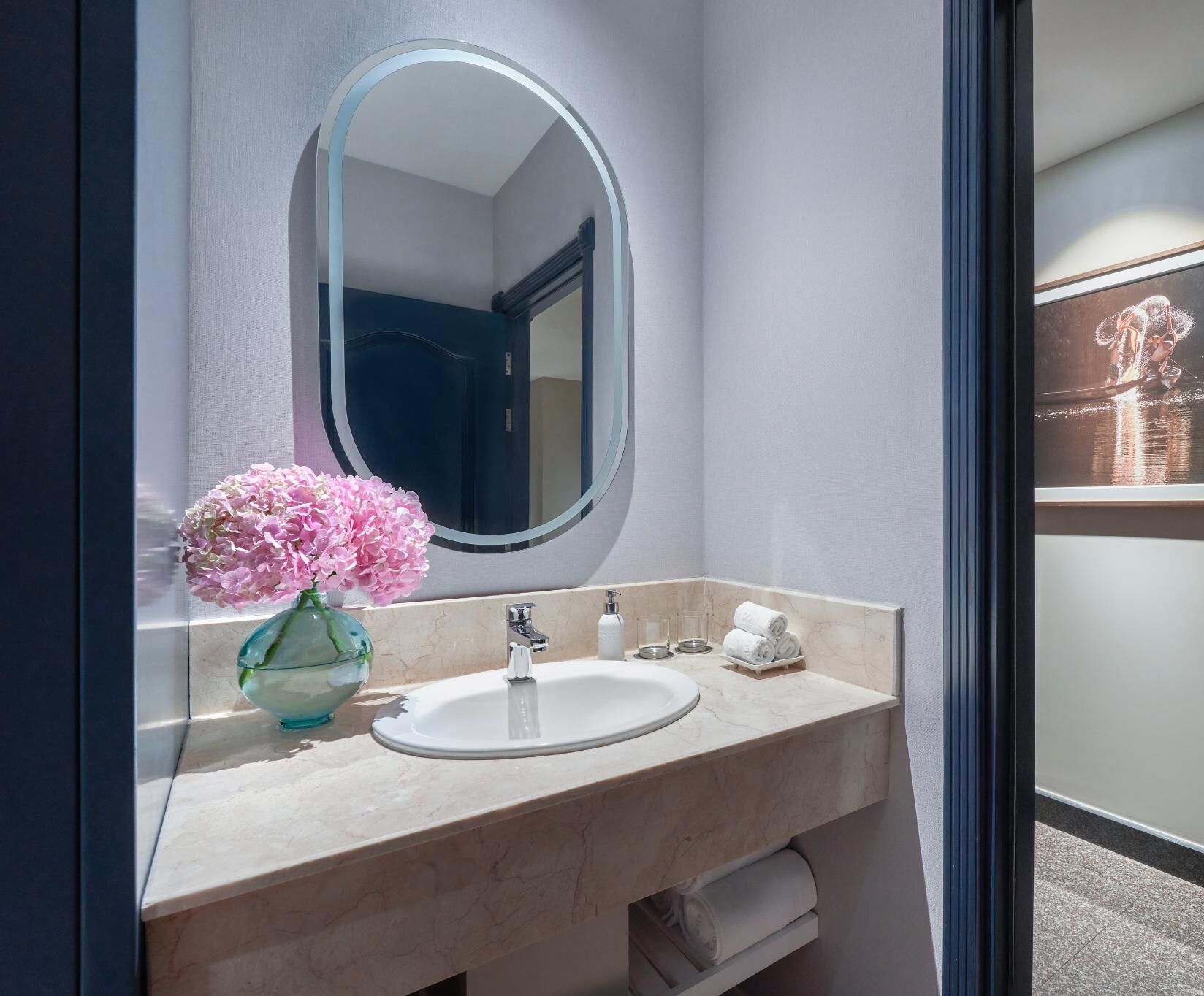 Un baño con lavamanos de mármol, un espejo, un florero y un perchero para toallas.