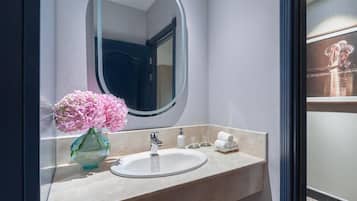 Un baño con lavamanos de mármol, un espejo, un florero y un perchero para toallas.