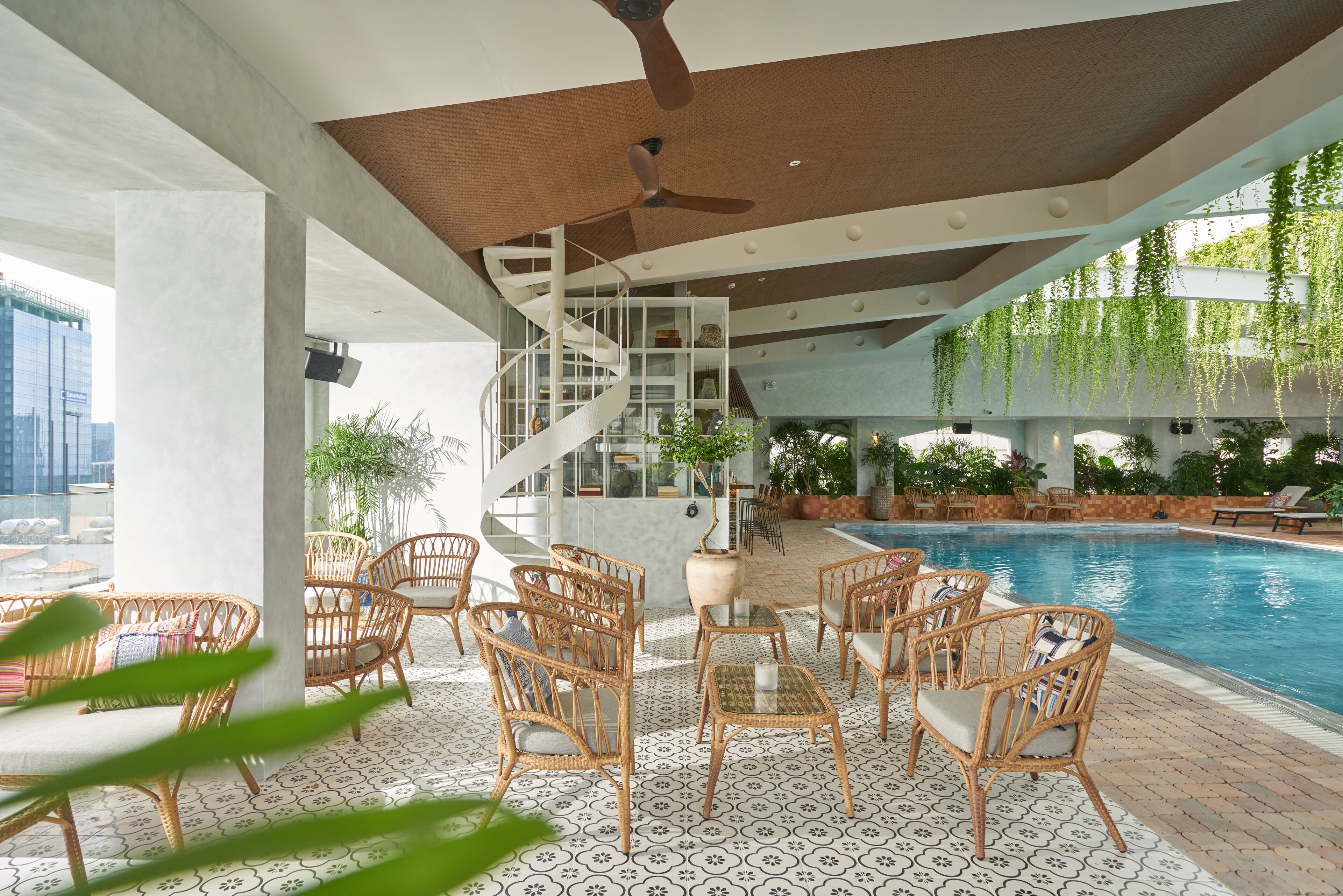 A poolside area with wicker furniture, a spiral staircase, and hanging plants.