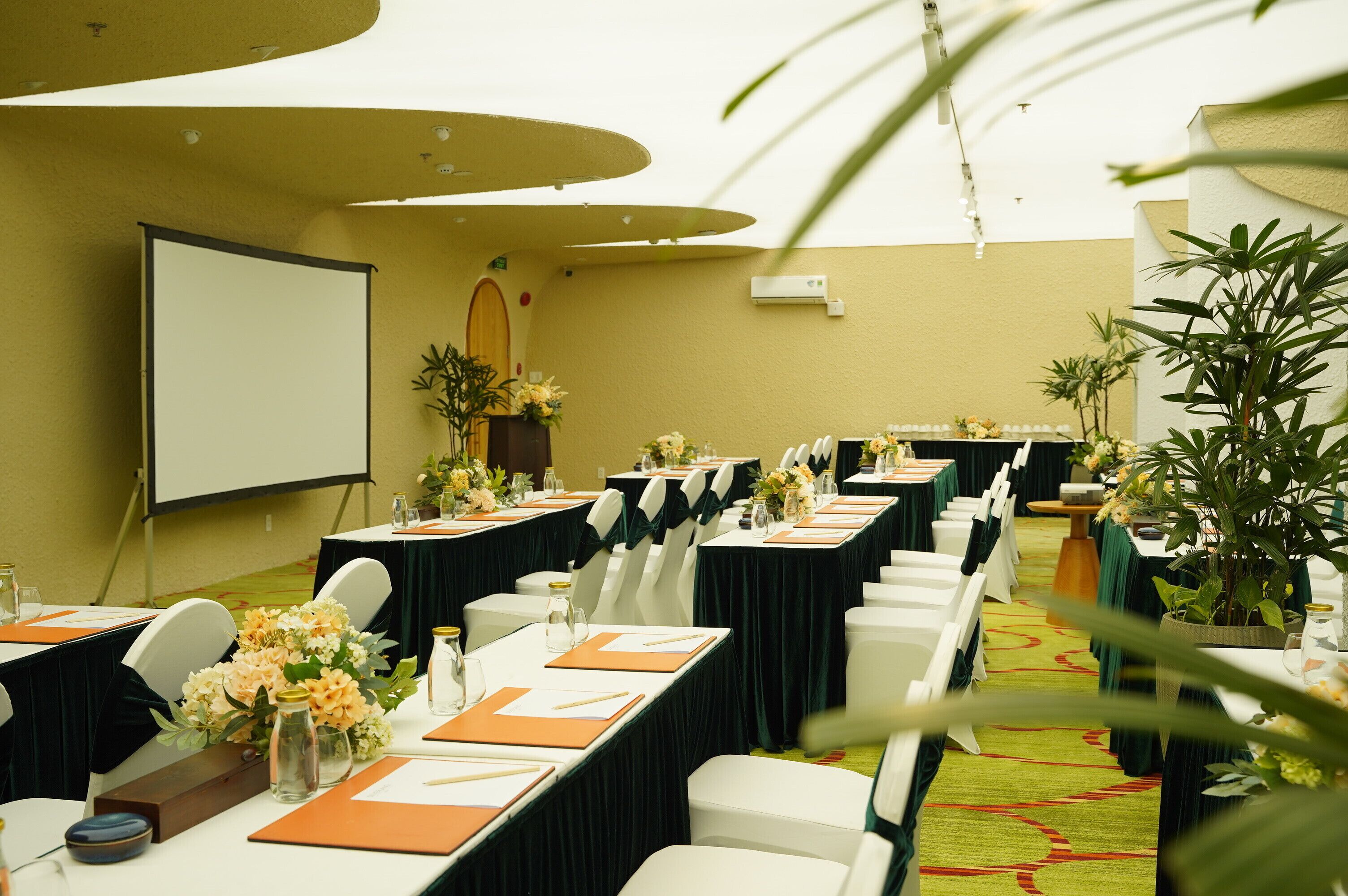 A conference room with rows of tables, chairs, and a projector screen.