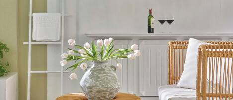 A room with a wicker ottoman, a white sofa, a bookshelf with decorative items, and a patterned floor.