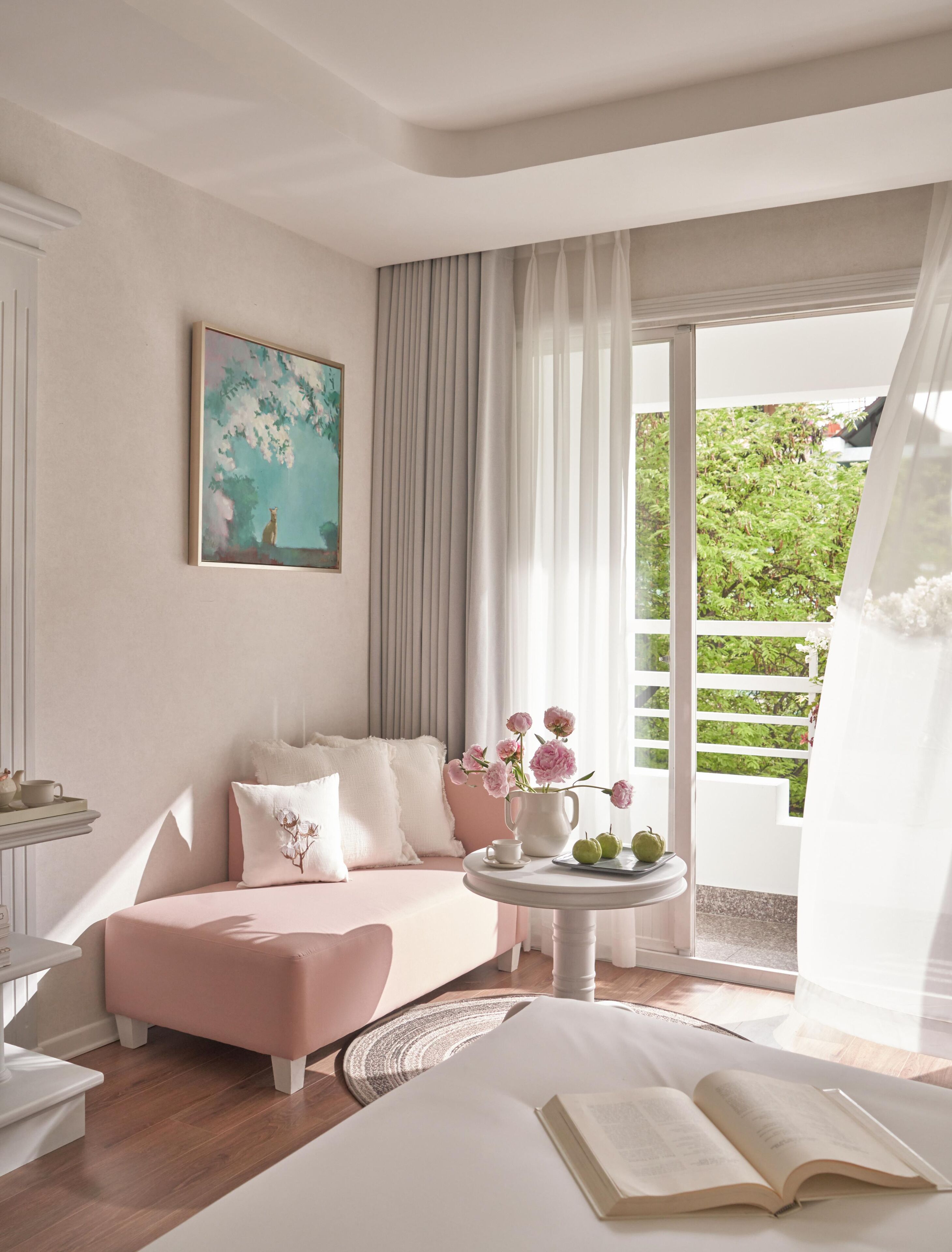A modern bedroom with a pink sofa, a round table with a vase of flowers, and a painting on the wall.