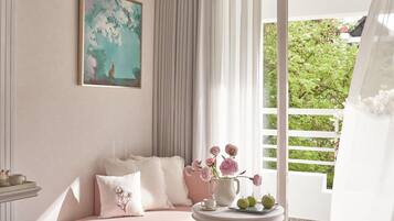 A modern bedroom with a pink sofa, a round table with a vase of flowers, and a painting on the wall.
