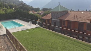 Ein Pool mit einer Steindeck, umgeben von einem eingezäunten Garten und Blick auf Berge.