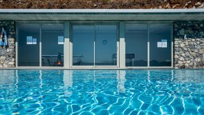 Ein Schwimmbecken mit klarem, blauem Wasser, einer Steinsäule und einem modernen Gebäude mit großen Glasfenstern.