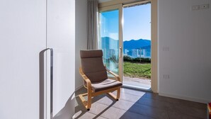 A room with a sliding glass door leading to a balcony, a wooden chair, and a view of mountains. - Dali in Spiglia With 2 Bedrooms and 1 Bathrooms (Parzanica)