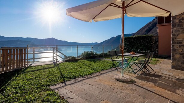 A patio with a table and chairs, a white umbrella, and a view of a lake and mountains. - Dali in Spiglia With 2 Bedrooms and 1 Bathrooms (Parzanica)