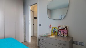 Ein Schlafzimmer mit einem Bett, einem Schminktisch, einem Spiegel und einer Tür zu einem anderen Raum.