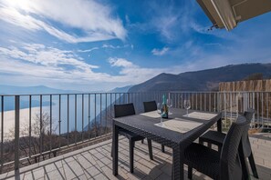 Un balcon avec une table et des chaises, donnant sur un plan d’eau et des montagnes.