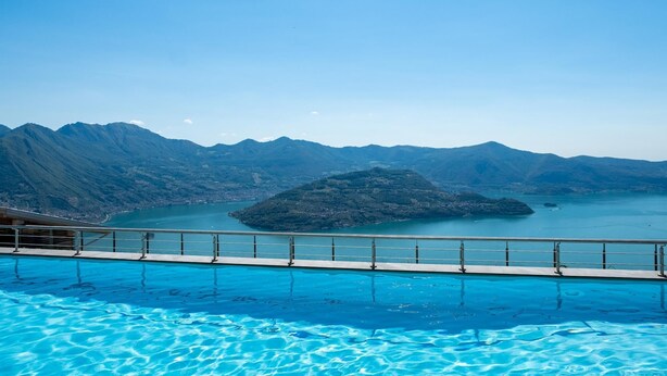 Ein Swimmingpool mit klarem, blauem Wasser, umgeben von Bergen und einer kleinen Insel im Hintergrund.