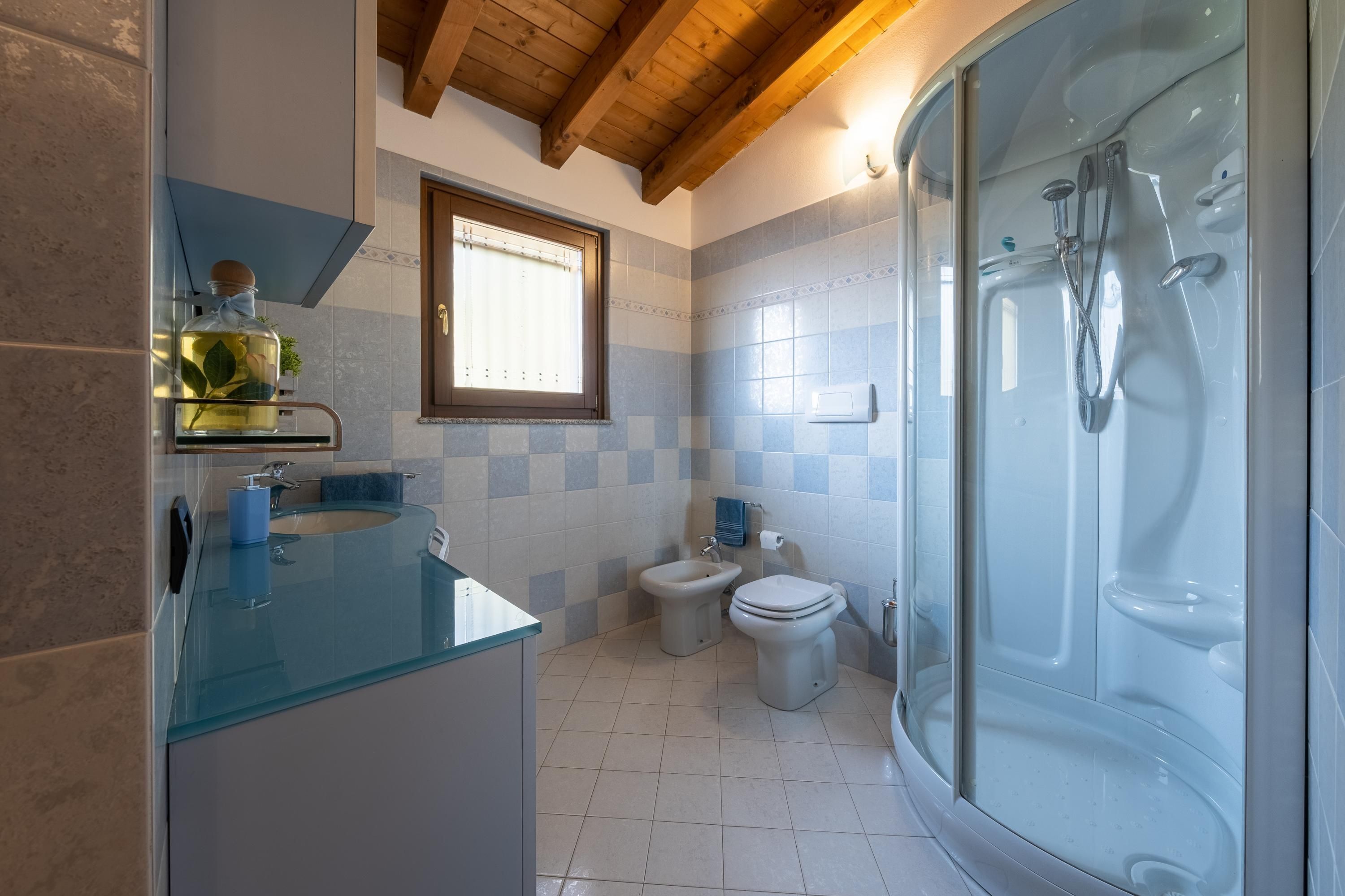 A modern bathroom with a glass shower enclosure, a glass sink, a bidet, and a toilet.
