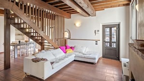 Ein großzügiger Wohnbereich mit einem weißen Sofa, einer Holztreppe und einer im Hintergrund sichtbaren Küche.