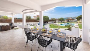 Un patio exterior con mesa, sillas y vista a una piscina y follaje.
